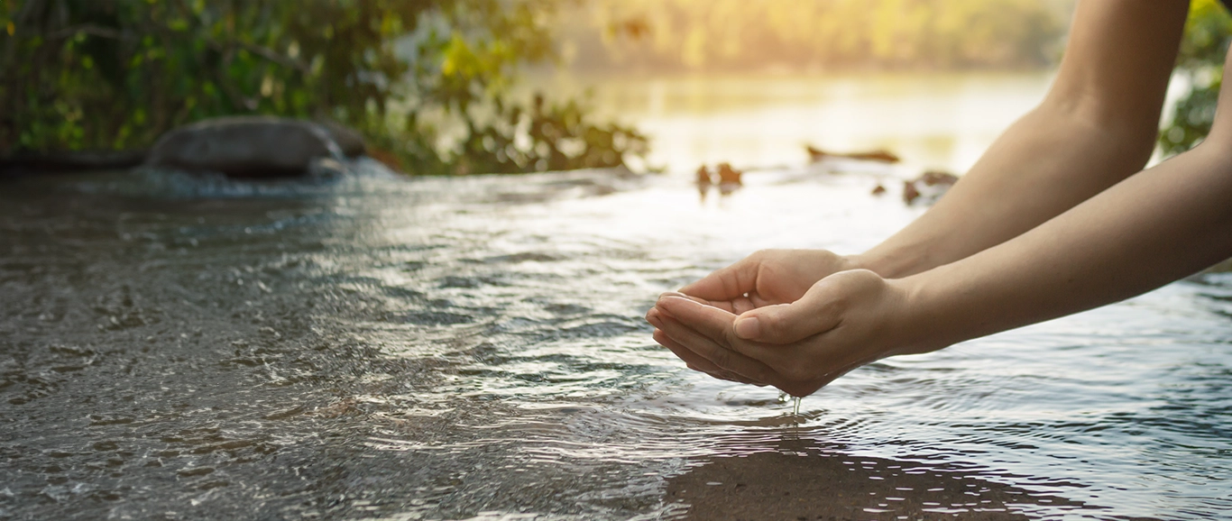 Mujer recolectando agua de un río en un entorno de exuberante paisaje verde