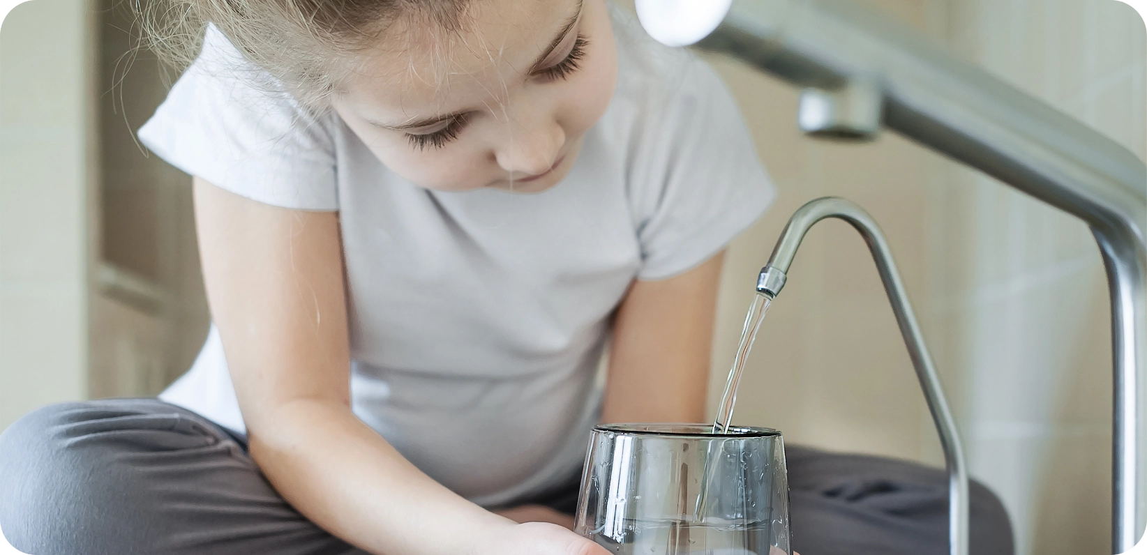 Una niña joven vierte agua en un vaso con una sonrisa en su rostro, mostrando alegría en el momento.