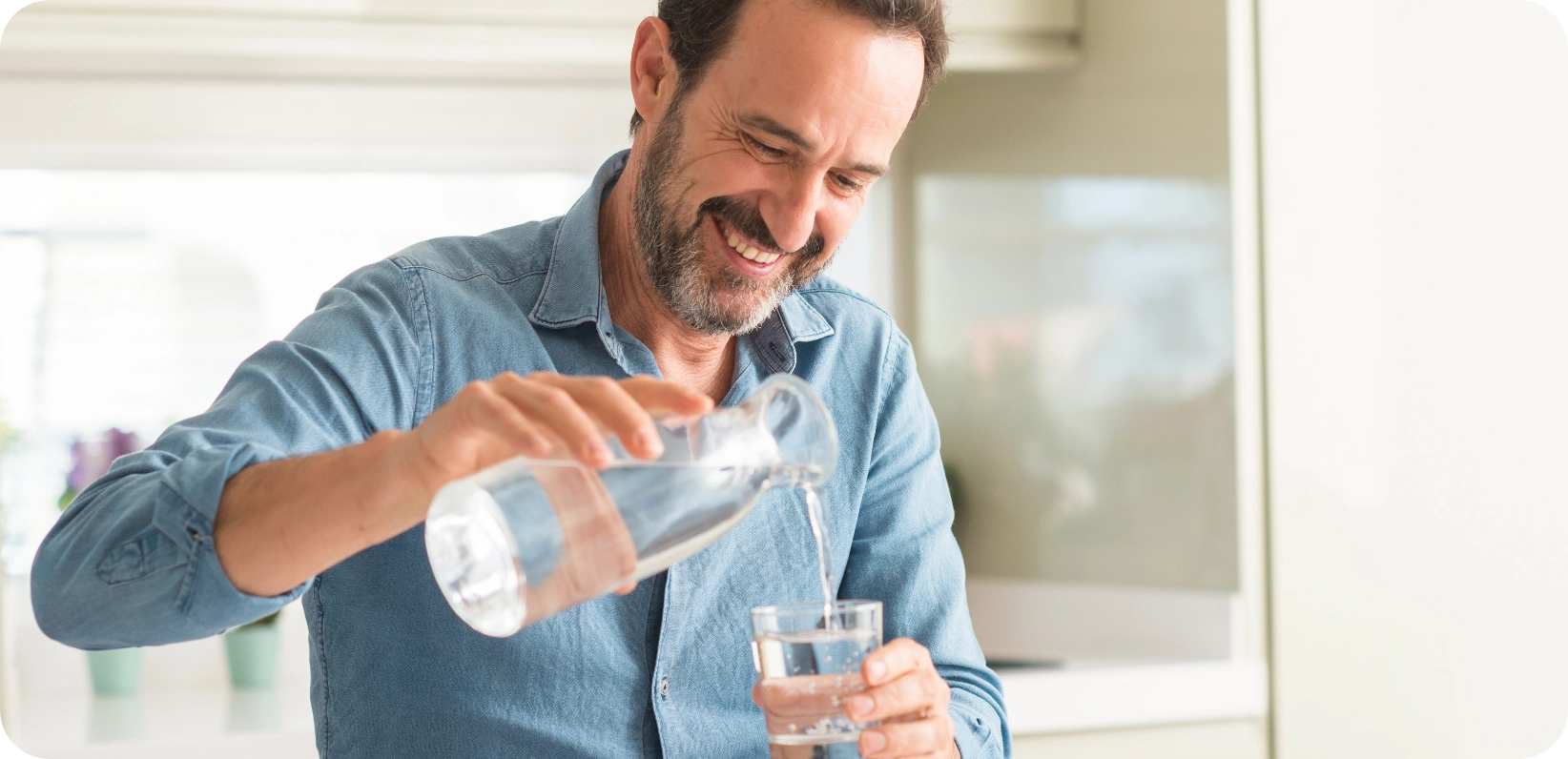 Hombre sonriente vertiendo agua en un vaso, transmitiendo alegría y frescura en un momento cotidiano.